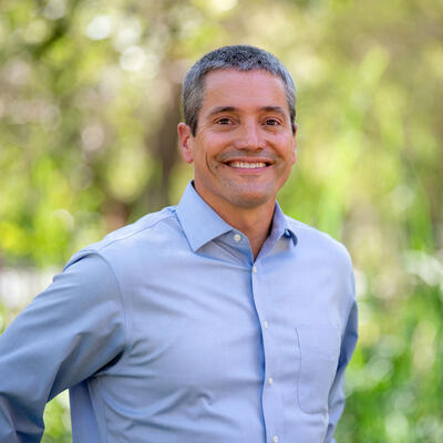 smiling man in blue shirt in front of lush green forest