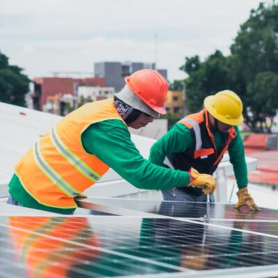 Two men working to install a solar panel on the roof of a building