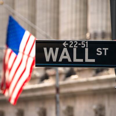 The street sign for Wall Street with an American flag in the background