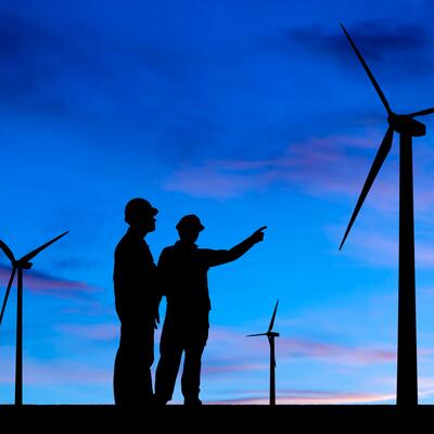 Two shillouted workers observe a wind farm